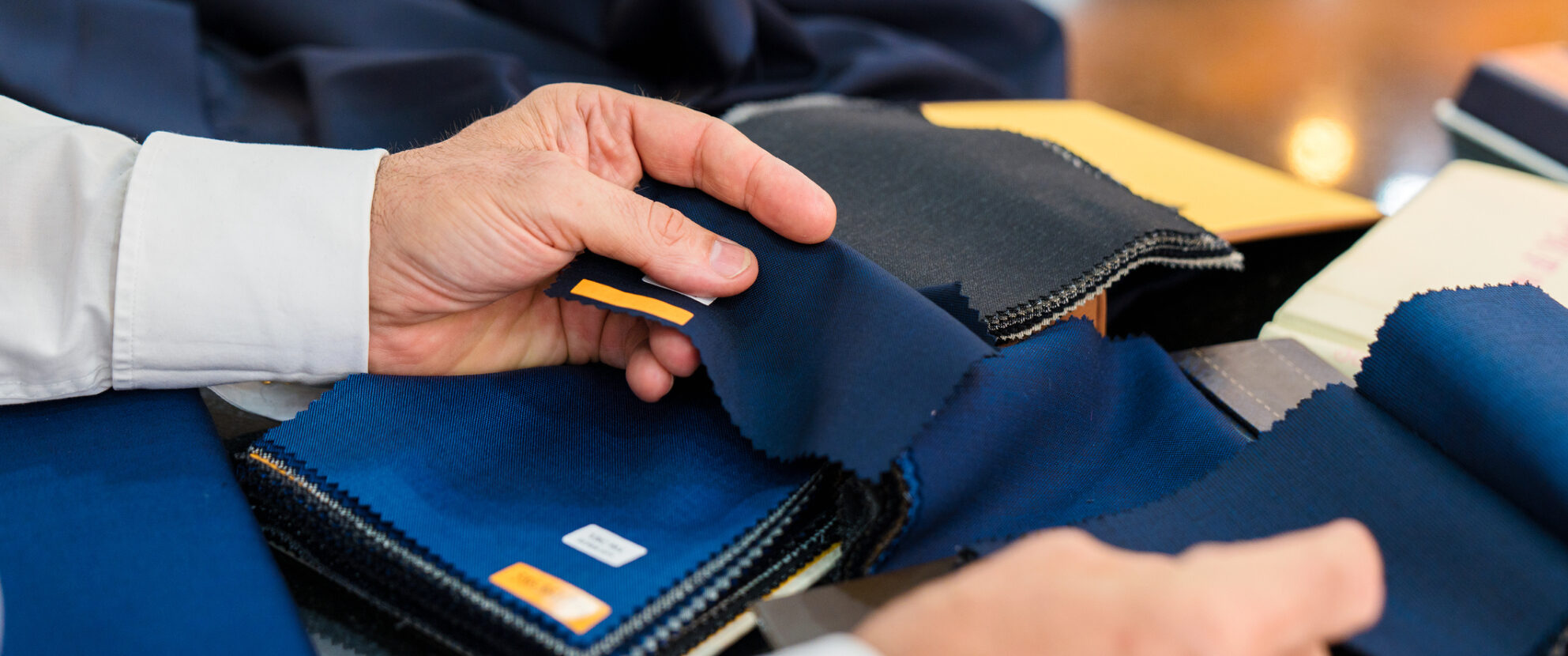 Mainline Custom Clothiers Style Sessions - Hands handling fabric samples for men's suits.